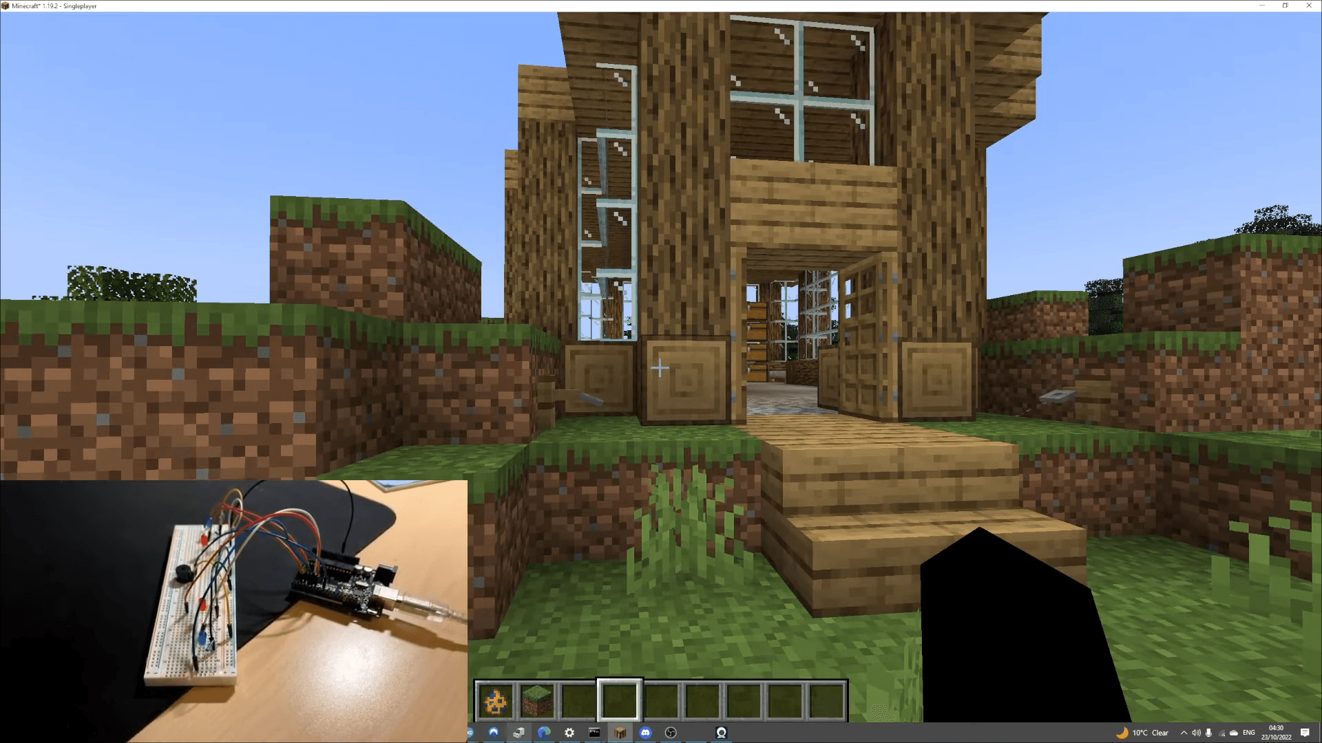 Minecraft home security project showing the in-game house entrance with the Arduino breadboard setup pictured in the corner